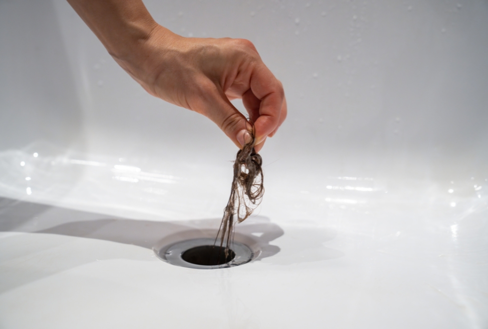 Plumber removing hair from a clogged bathroom drain, showing common causes of blocked drains and the need for professional drain cleaning, hydro jetting, and clogged drain repair by Neighborhood Plumbing. Reach out today for help with what will dissolve a blocked drain, best drain cleaner for clogged drains, how to unclog a drain, dissolve hair in drain, how to dissolve grease in drain pipe, unclog shower drain, clogged sink drain solutions, chemical drain cleaners, natural drain unclogging methods, hydro jetting service, drain cleaning service, emergency drain cleaning, drain repair near me, local plumber for drain blockage, slow drain fix near me, drain unclogging services near me, pipe cleaning services, plumbing services near me, clogged drain plumber near me, kitchen drain cleaning, bathroom drain cleaning, professional drain unclogging, drain line cleaning near me, affordable drain repair.